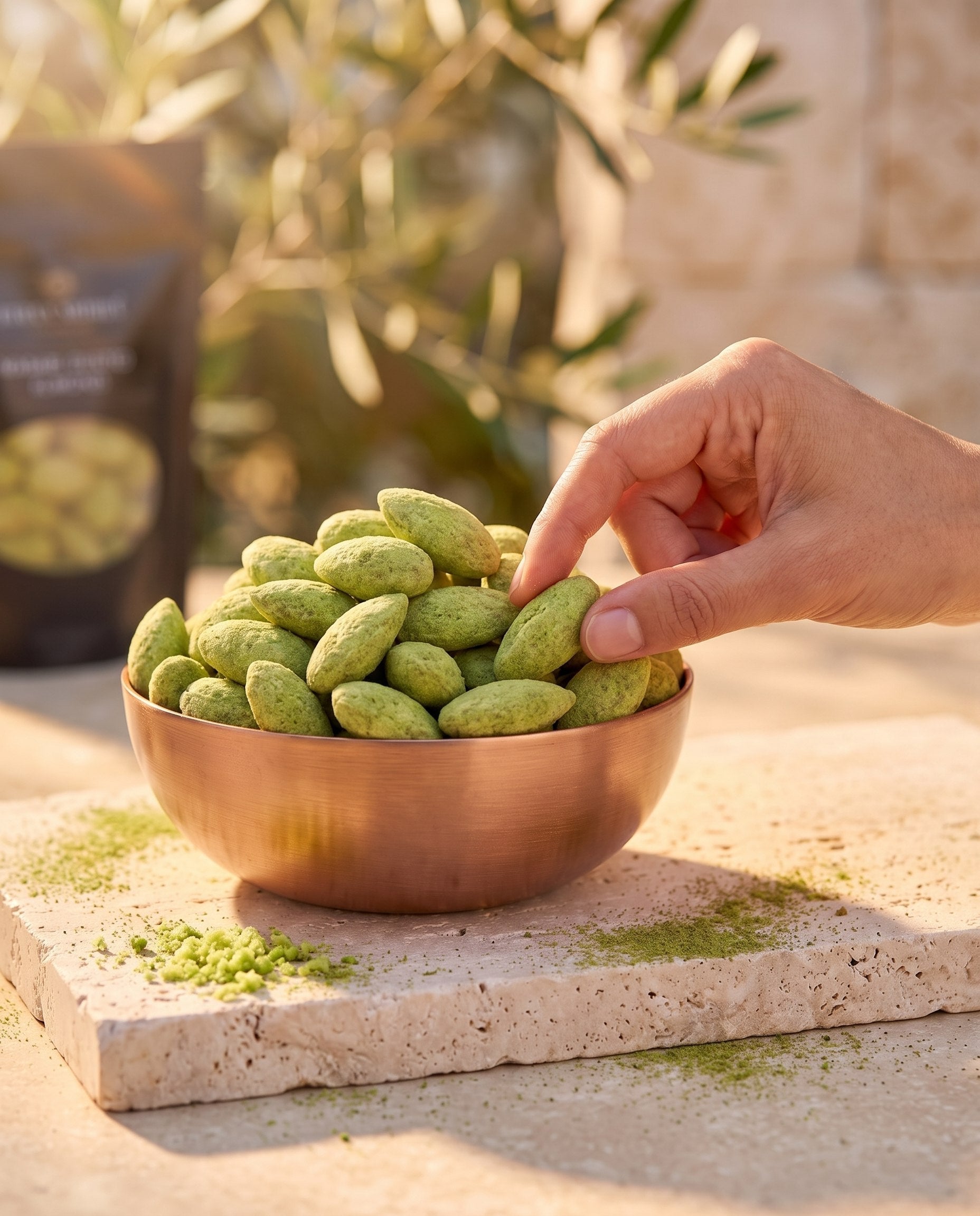 Amande Wasabi, moment thé vert, main prélevant une amande dans un bol de cuivre sur pierre claire