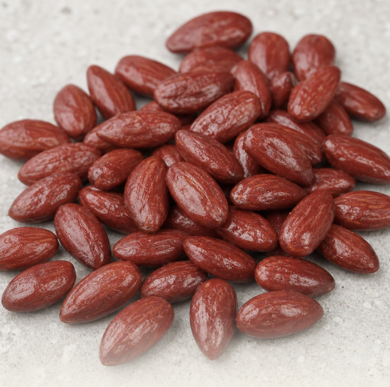 Amandes Framboise à l’enrobage brun-rouge satiné, matière en gros plan sur pierre grise claire