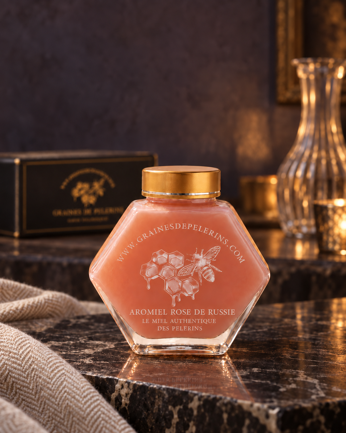 Frasco de Aromiel Rose sobre piedra oscura reflectante, junto a un tejido de lana, con un estuche detrás.