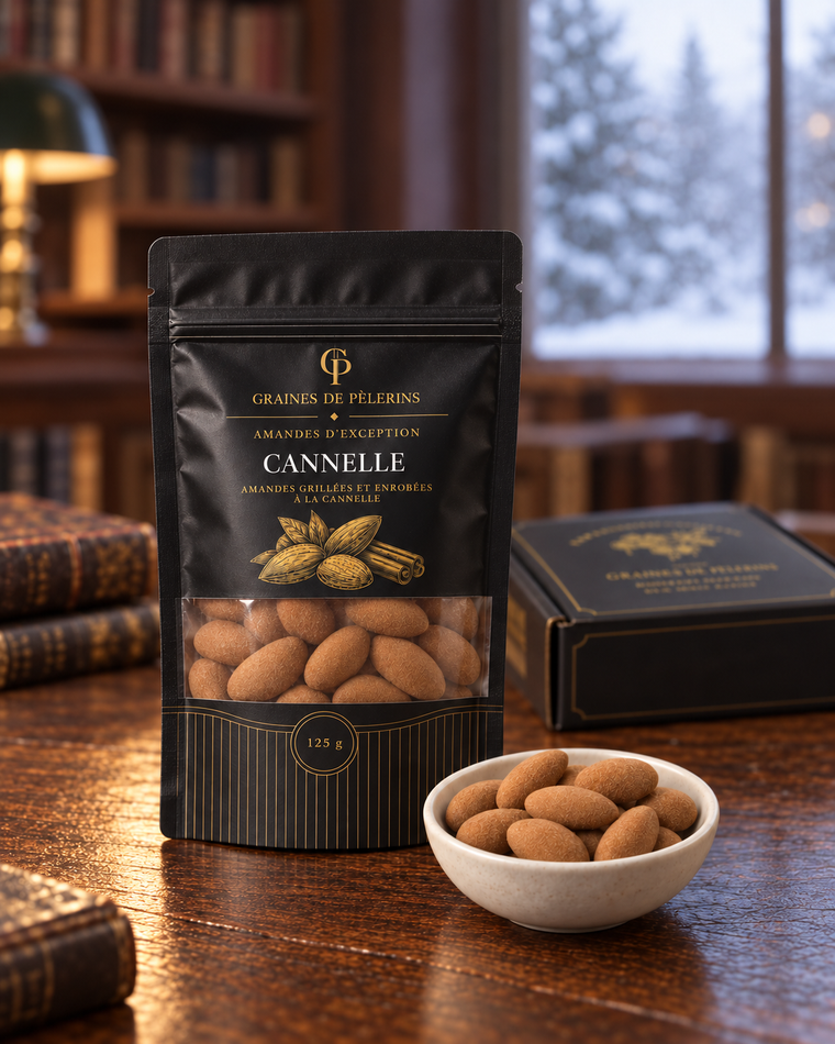 Amandes Cannelle, leur présentation noire et or et une coupelle, dans une bibliothèque hivernale avec un coffret en arrière-plan.