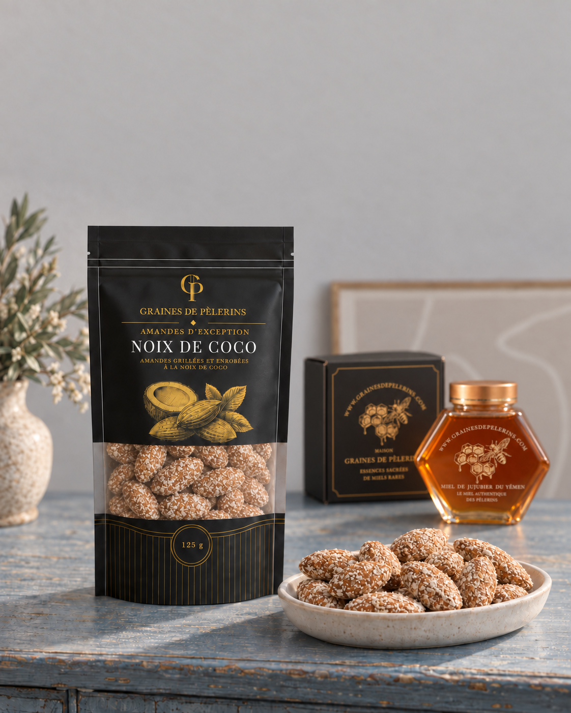 Sachet et coupelle d’amandes Noix de Coco sur une console bleue, avec un miel de Jujubier et son écrin en arrière-plan.