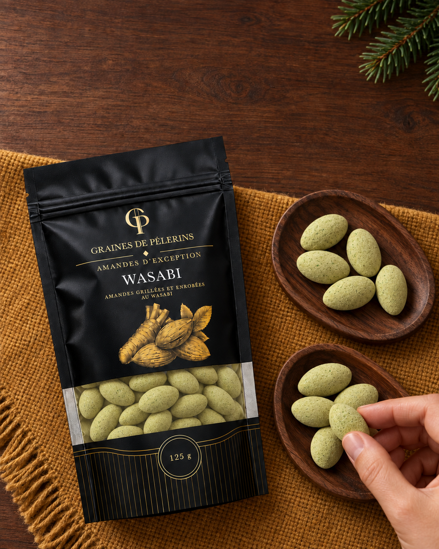 Eine Hand nimmt eine Wasabi-Mandel aus einer Schale neben dem Beutel auf ockerfarbenem Stoff.