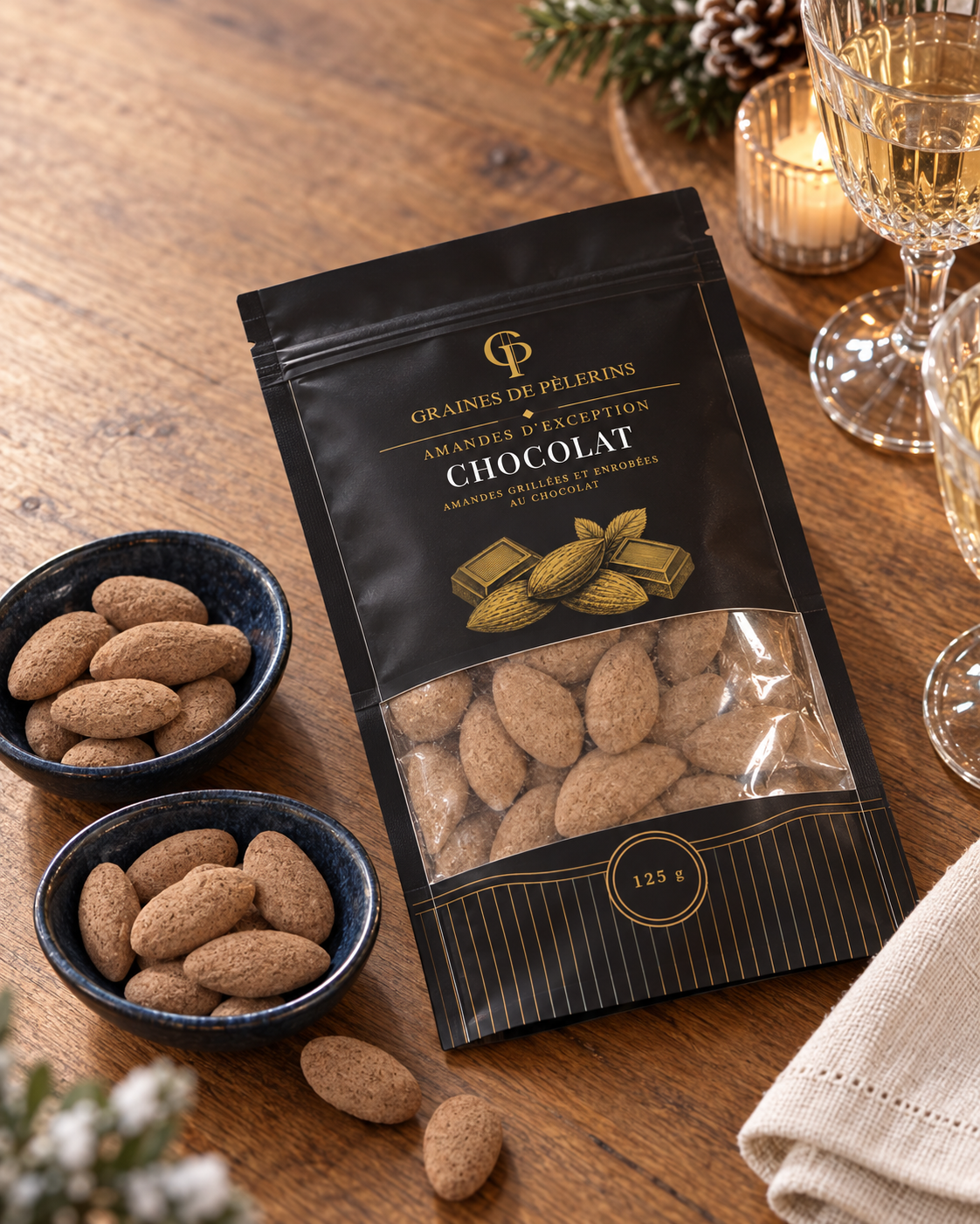 Amandes Chocolat présentées avec deux coupelles bleues sur une table en bois, du lin clair, des verres taillés et une bougie, vues en plongée.