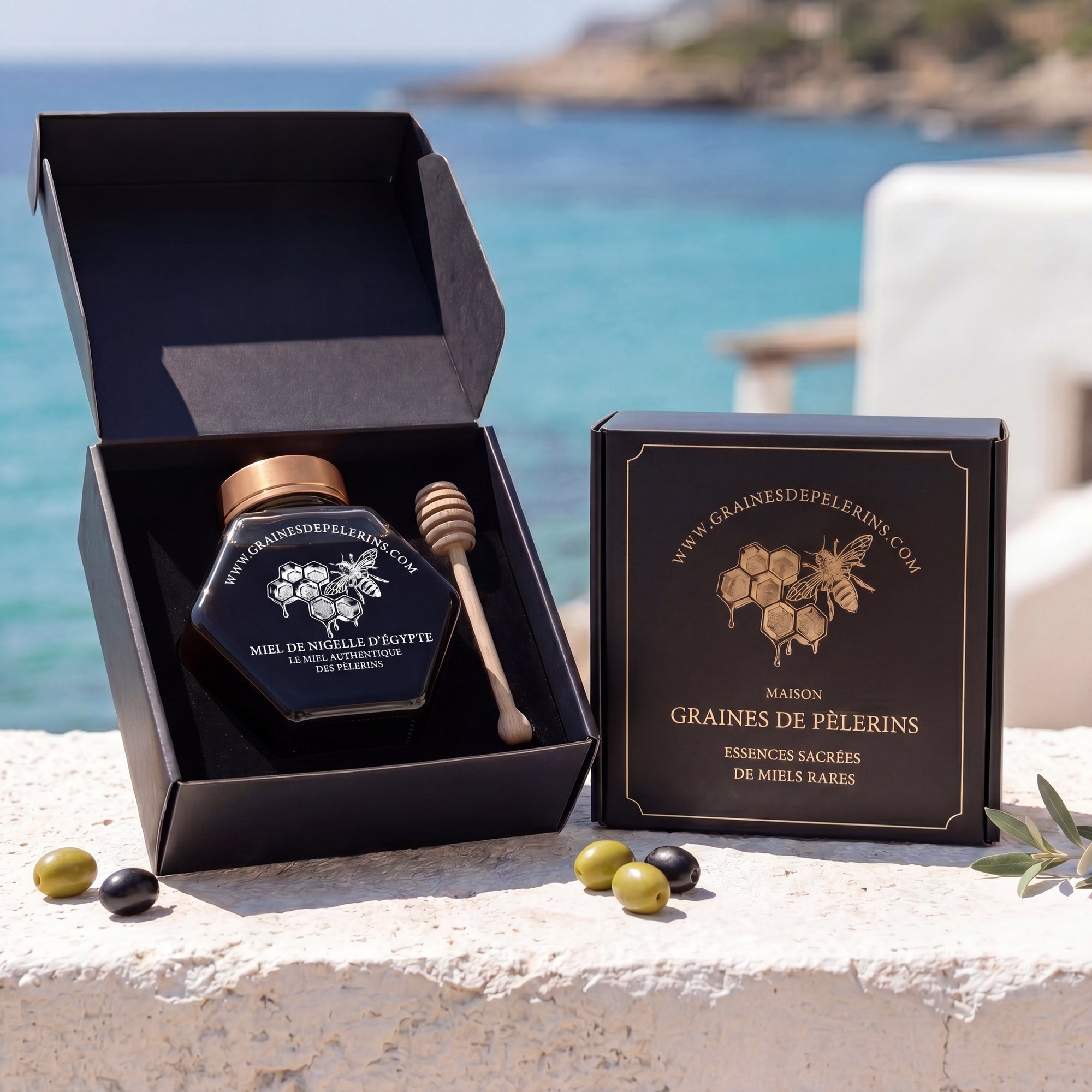 Écrin noir ouvert du Miel de Nigelle avec pot actuel et cuillère de dégustation face à la côte